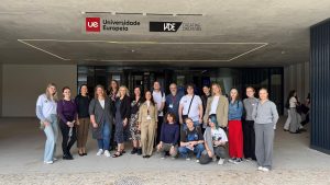 Group photo of students and staff posing in front of the Universidade Europeia / IADE – Creating Creators building entrance; the group stands under the campus sign, smiling toward the camera.