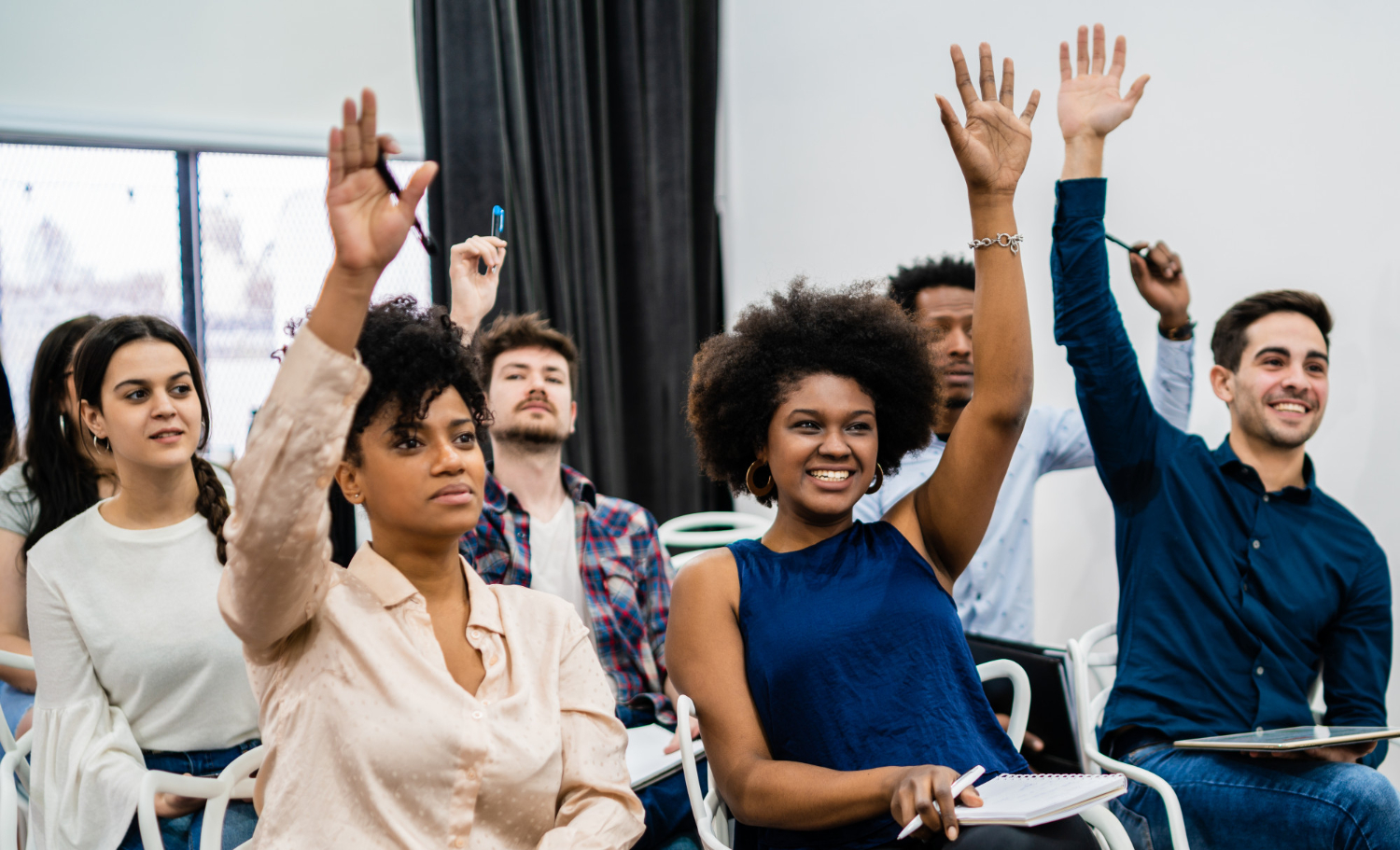 Fot. Freepik.com/mego-studio Students in a classroom raising their hands, smiling and engaged, some holding notebooks and pens