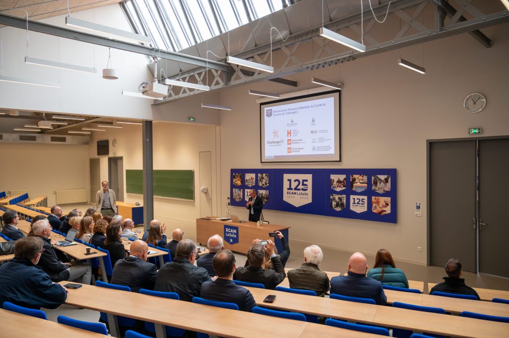 Lecture at ECAM LaSalle: presenter at a podium addressing attendees; ‘125 ans’ banners and partner logos on the screen
