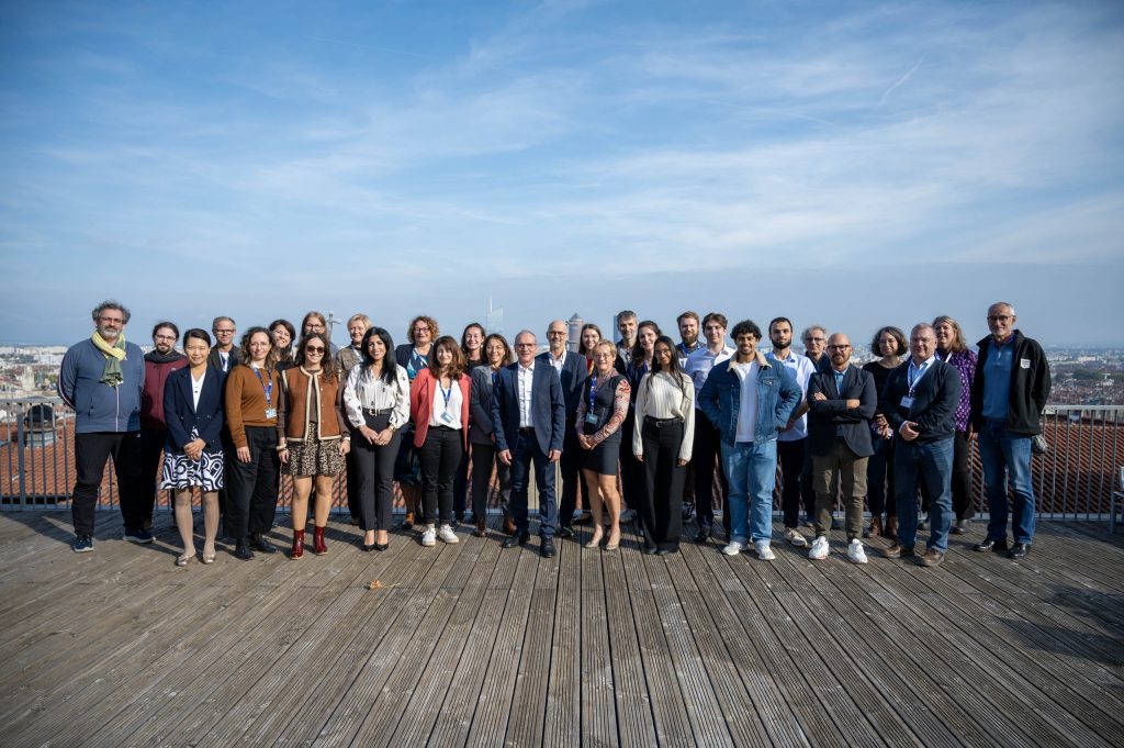 Large group portrait on a rooftop terrace in Lyon with blue sky and city views in the background
