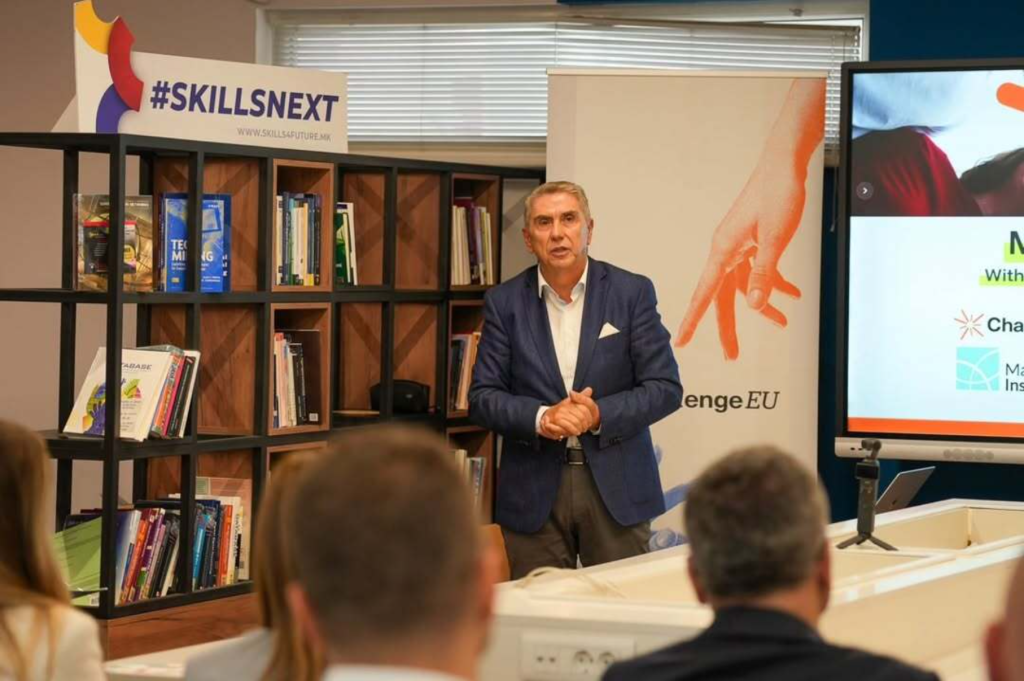 eynote speaker addresses participants in front of a ChallengeEU banner and #SKILLSNEXT bookshelf during the university–industry forum.