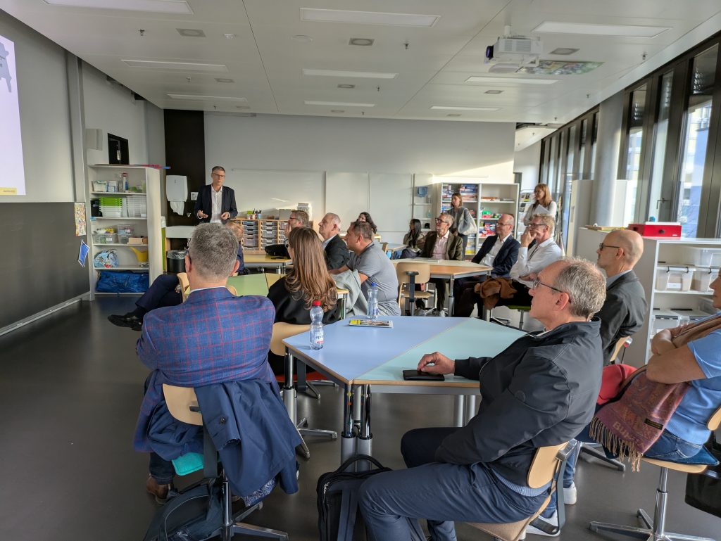 Audience of university leaders seated at tables during a presentation at FHNW; speaker stands by a screen at the front of the room