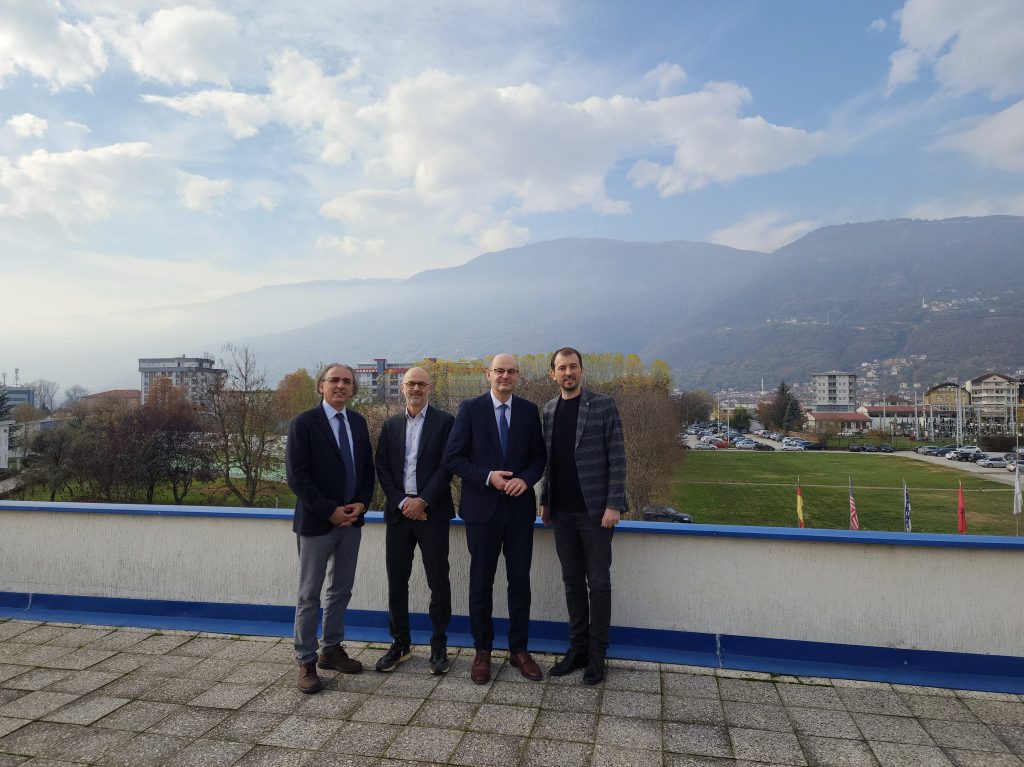 Four representatives from SEEU and Hochschule Offenburg standing outside on a terrace with a mountainous landscape and the city in the background, posing for a group photo.

