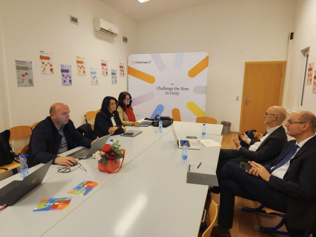 Representatives from SEEU and Hochschule Offenburg sitting at a meeting table with laptops and ChallengeEU materials, during a working session in a room with ChallengeEU branding on the back wall.