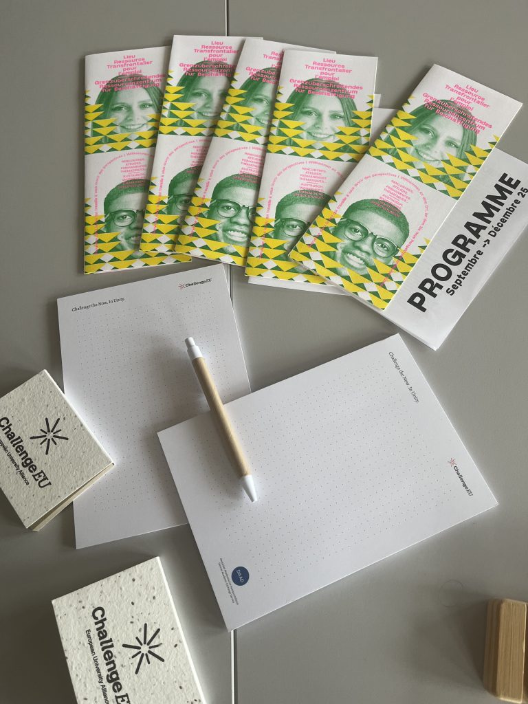 Table with colourful workshop brochures, ChallengeEU-branded notepads and a pen prepared for Sustainable Idealab participants.