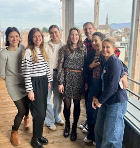 Group photo of seven Sustainable Idealab team members and participants smiling on a wooden balcony with the city and hills in the background.