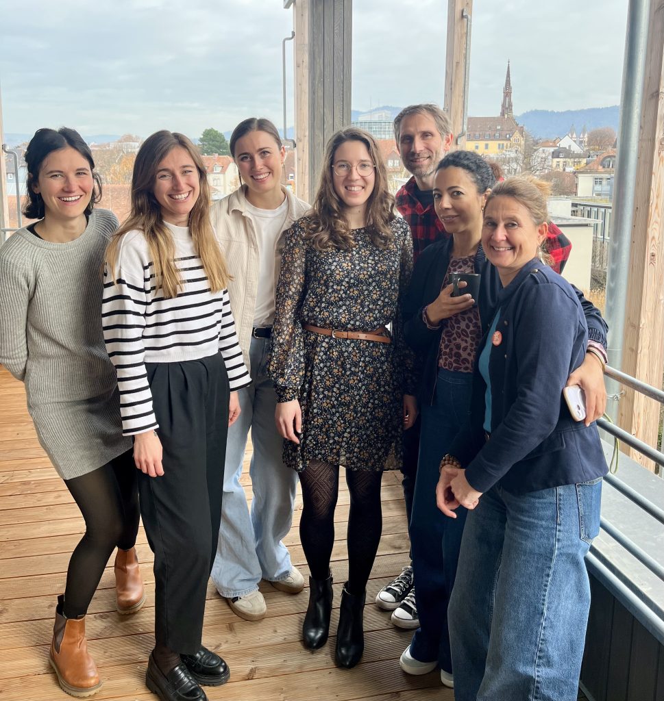 Group photo of seven Sustainable Idealab team members and participants smiling on a wooden balcony with the city and hills in the background.