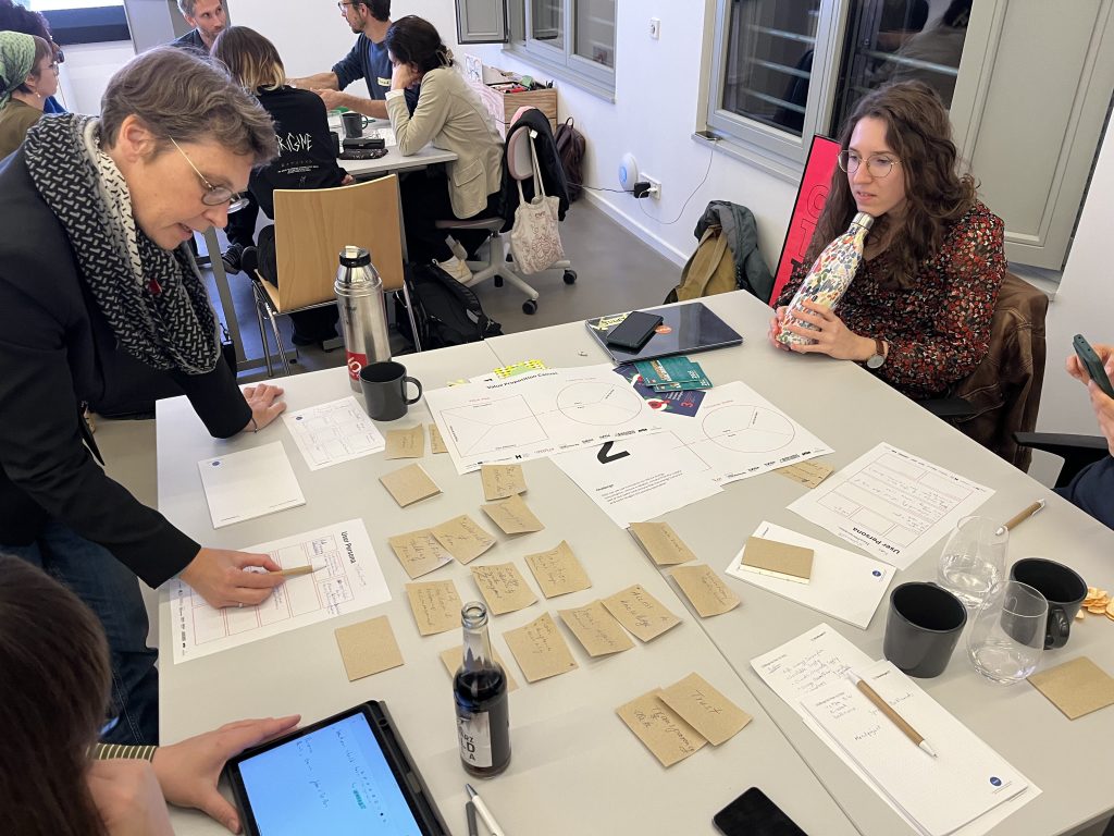 Small group of participants working around a table covered with worksheets and cardboard notes, discussing ideas during a co-creation exercise.