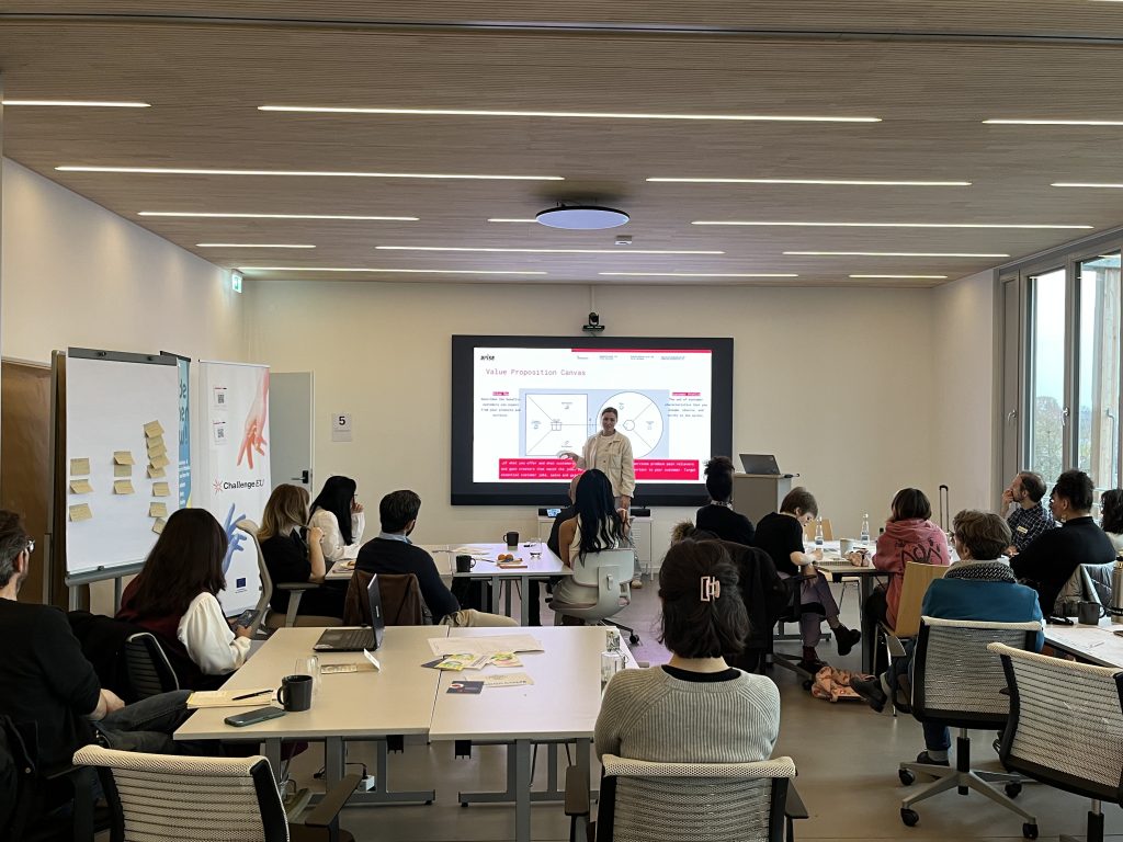 Facilitator explaining the Value Proposition Canvas on a large screen while workshop participants sit in groups and take notes.