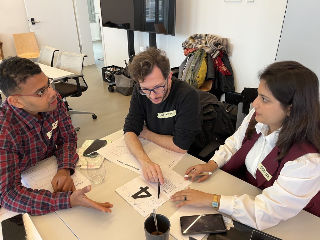 Three workshop participants in discussion at a table, pointing to a Value Proposition Canvas sheet and brainstorming their challenge solution.