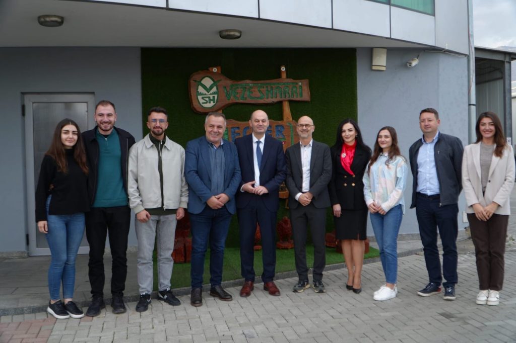Group photo of representatives from Hochschule Offenburg, South East European University and Veze Sharri standing in front of the Veze Sharri company building and logo