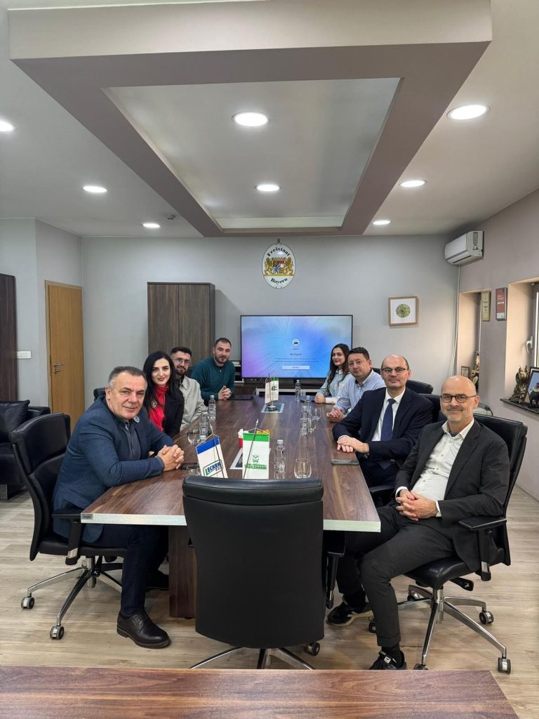 Representatives from Hochschule Offenburg, South East European University and Veze Sharri seated around a large conference table during a meeting, with flags and a presentation screen visible in the background.