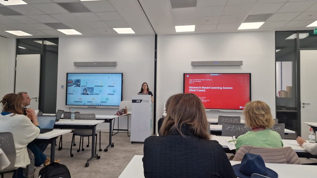 Academic staff attend a Challenge Based Learning training session in a modern lecture room, listening to a presentation with slides displayed on large screens.