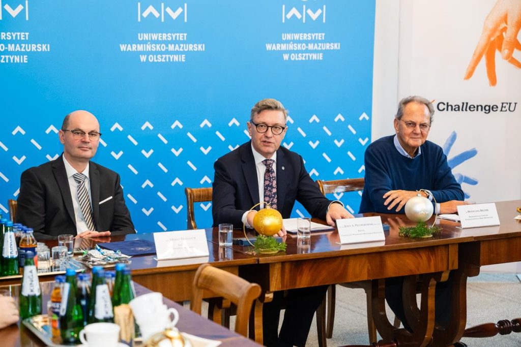 Three representatives sit at the main table during the UWM–HSO meeting, with UWM and ChallengeEU banners in the background and festive ornaments decorating the table.