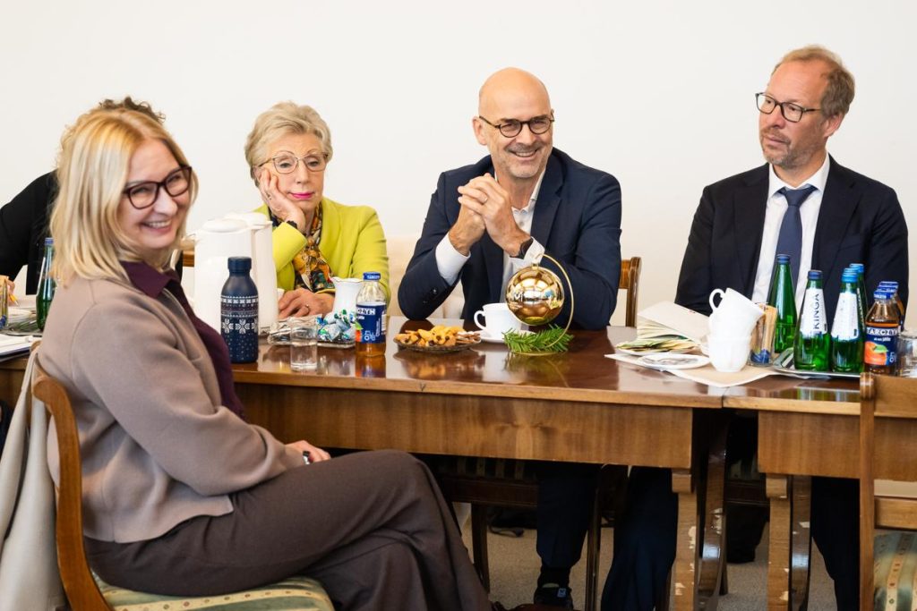 Participants seated at a meeting table smile and listen, with refreshments and a small Christmas decoration on the table.