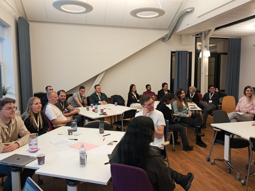 Participants seated around tables during a ChallengeEU workshop session, listening and discussing with notes and coffee cups on the tables.