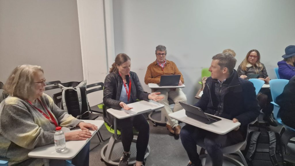 Small group discussion during a Challenge Based Learning workshop, with participants exchanging perspectives and using digital devices.