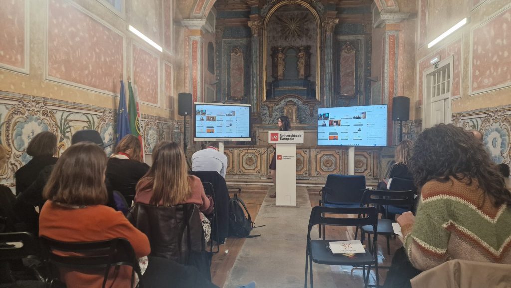 Audience seated in a historic lecture hall while a presenter speaks at the front of the room during an academic event.