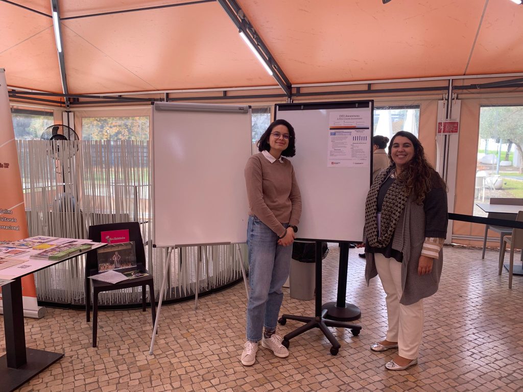 The picture shows two women standing near the table during the public engagement event at the Universidade Europeia de Lisboa.