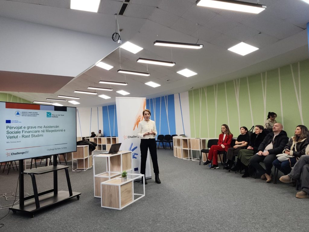 A presenter from SEEU stands next to a screen displaying a case study on the experiences of women using social assistance in North Macedonia; in front of her sits a group of participants attending the ChallengeEU seminar.