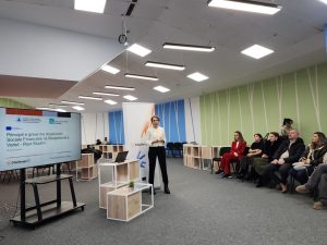 A presenter from SEEU stands next to a screen displaying a case study on the experiences of women using social assistance in North Macedonia; in front of her sits a group of participants attending the ChallengeEU seminar.