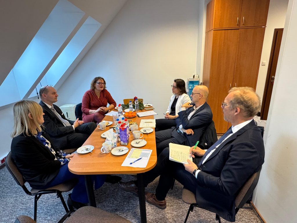 Small working meeting in an office: six participants sit around a table with notes, documents and coffee, discussing next steps.