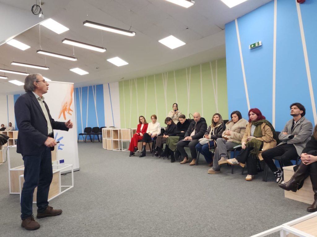 A speaker delivers a lecture as part of a ChallengeEU event, addressing a group of participants seated in a semi-circle in the workshop room.