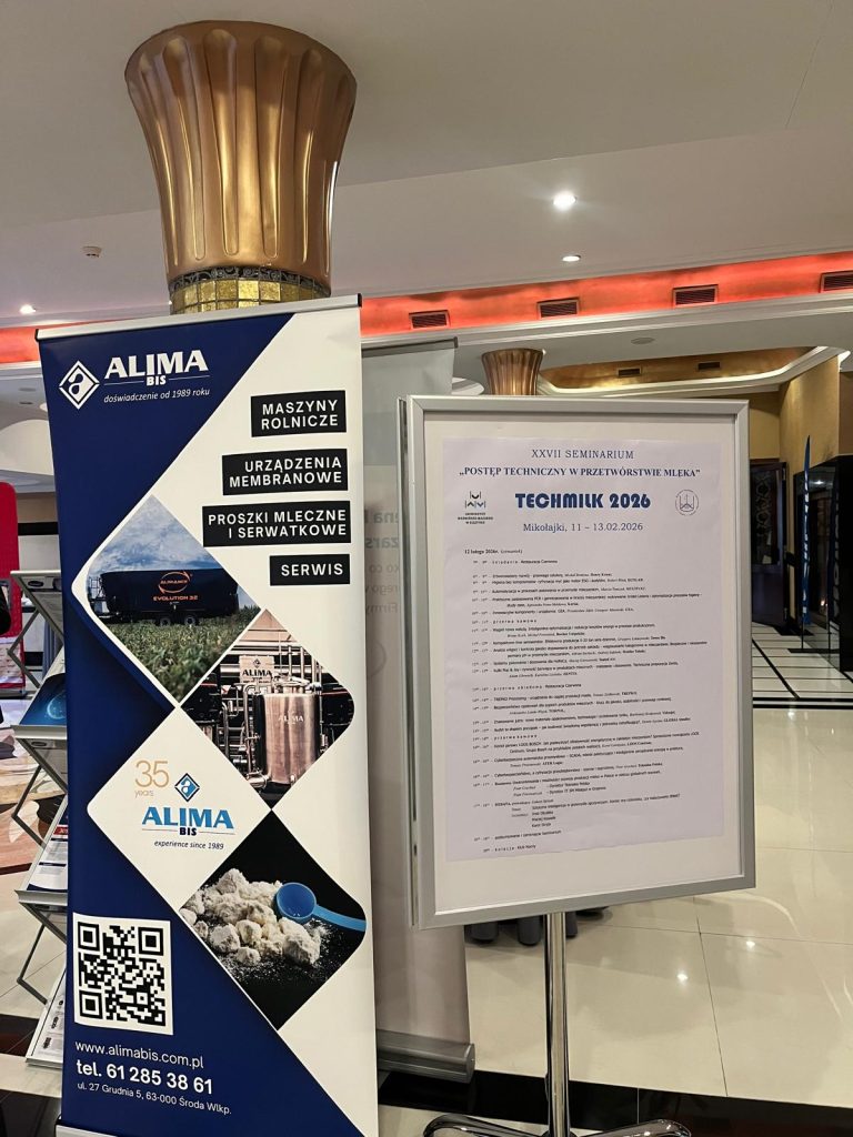 Information stand at the Techmilk 2026 seminar with event programme board and exhibitor banner in the background.