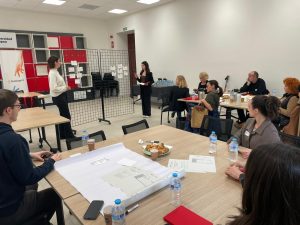Participants attend the M.A.R.K.E.T. Meet-Up workshop on Events and Sustainability, engaging in group discussions around tables while two facilitators present ideas at the front of the room.