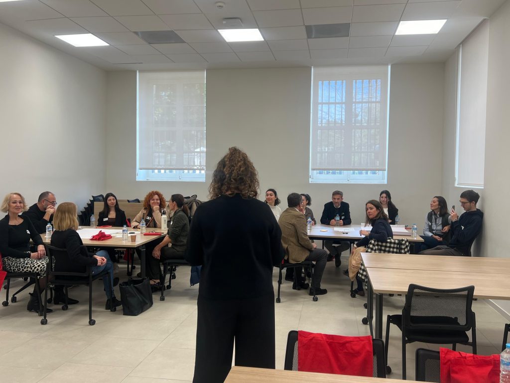 Participants seated around tables listen to a facilitator during the M.A.R.K.E.T. Meet-Up on Events and Sustainability in the Region of Valencia in a bright meeting room.