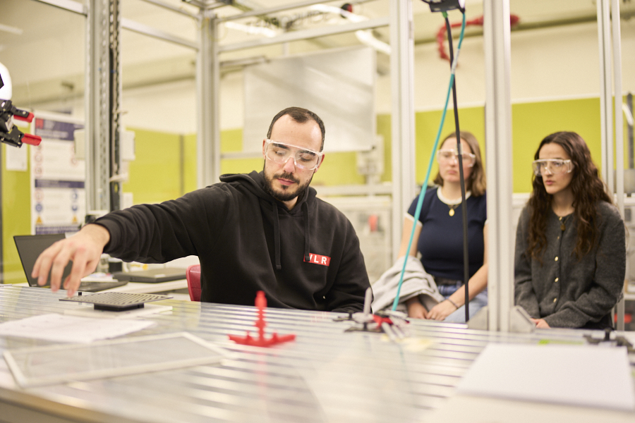 A WLRI staff member demonstrates a robotics process while students observe from behind a safety barrier in the laboratory.