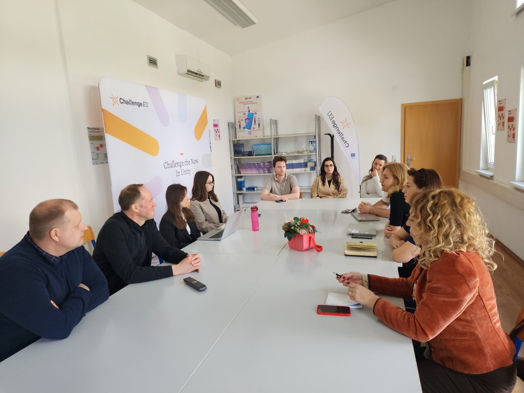 Participants seated around a table during a meeting, engaged in discussion in a room with ChallengeEU branding visible in the background.