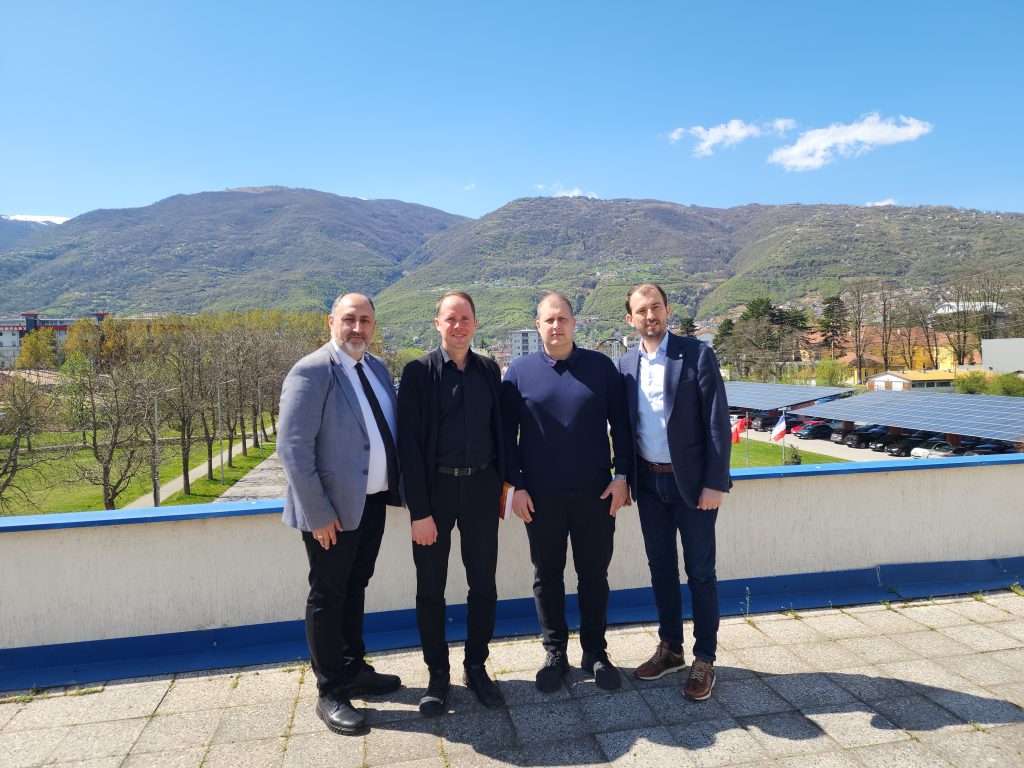 Four men standing outdoors on a terrace with a mountainous landscape in the background during an official visit.