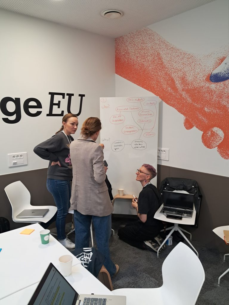 Three participants discussing ideas around a flipchart with notes on target groups and stakeholders during a collaborative WP4 session.
