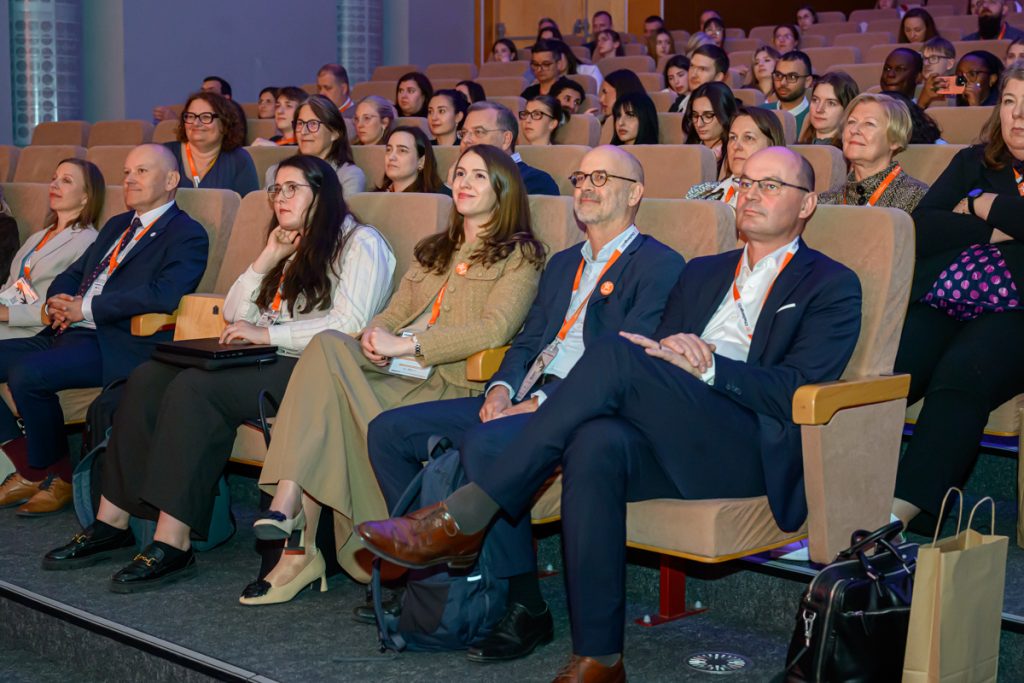 Conference guests wearing ChallengeEU lanyards sit in the auditorium and listen during the opening session.