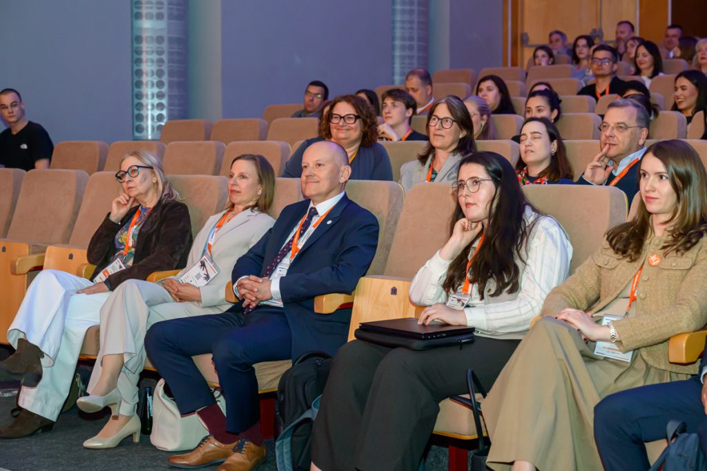 Conference guests wearing ChallengeEU lanyards sit in the auditorium and listen during the opening session.
