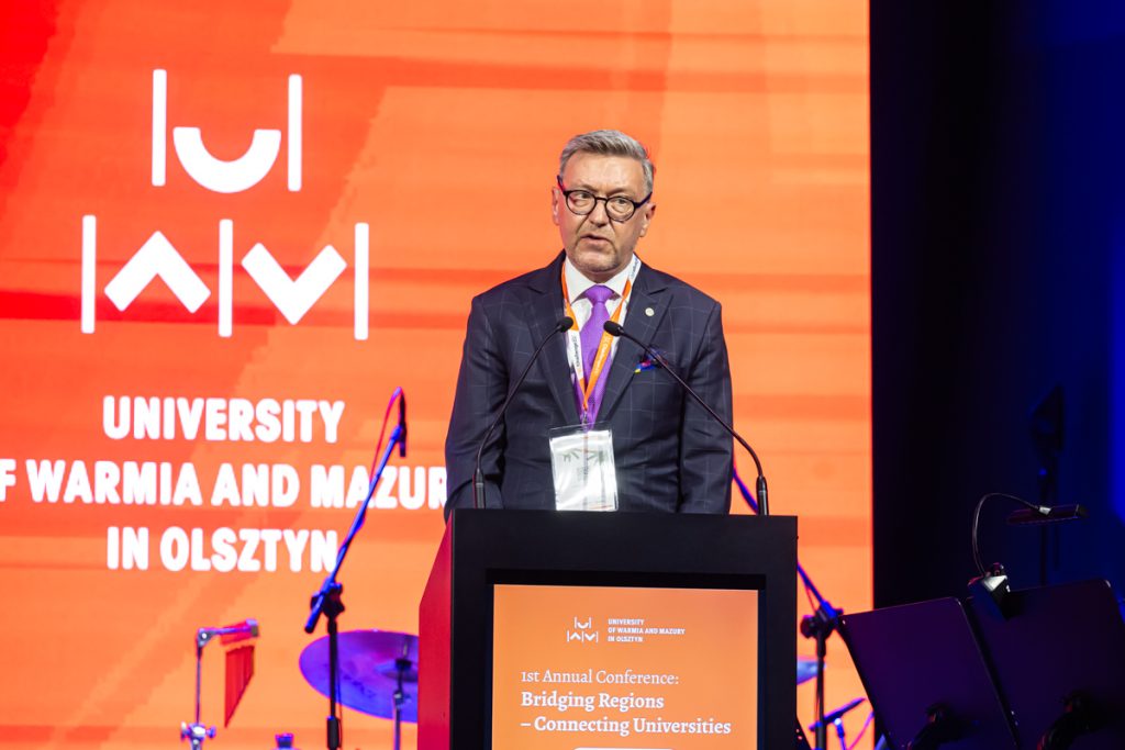 Jerzy Przyborowski stands at the podium during the ChallengeEU 1st Annual Conference opening session, with a large UWM logo behind him.