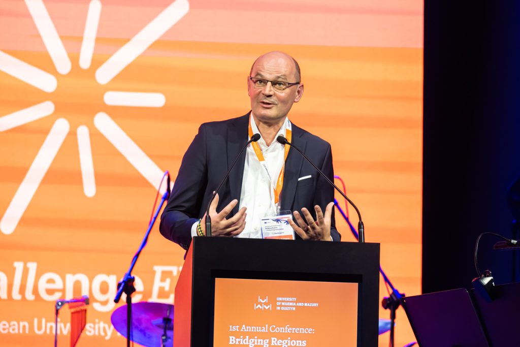 A speaker stands at the podium during the ChallengeEU 1st Annual Conference opening session, with a large ChallengeEU screen behind him.