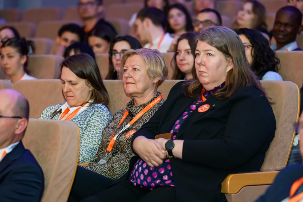 Conference guests wearing ChallengeEU lanyards sit in the auditorium and listen during the opening session.