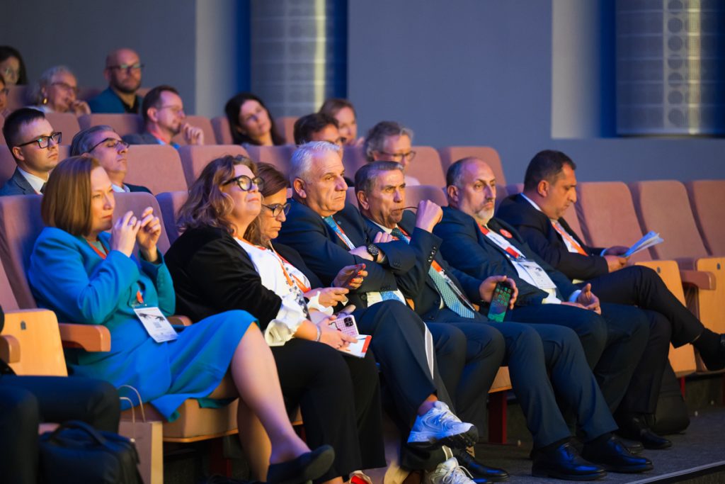 Conference guests wearing ChallengeEU lanyards sit in the auditorium and listen during the opening session.