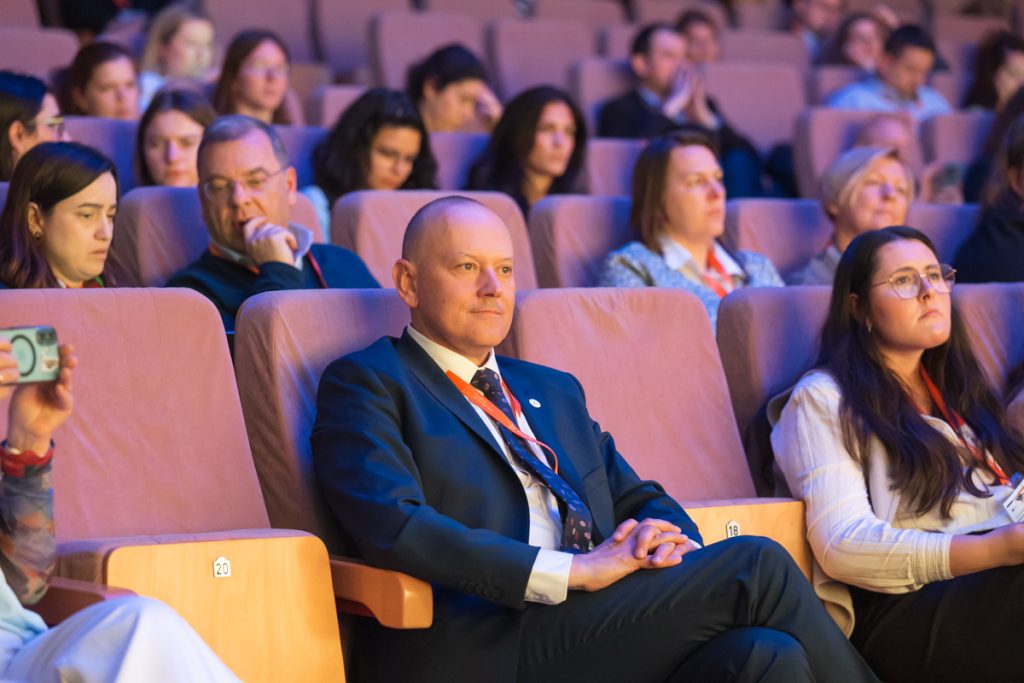 Conference guests wearing ChallengeEU lanyards sit in the auditorium and listen during the opening session.