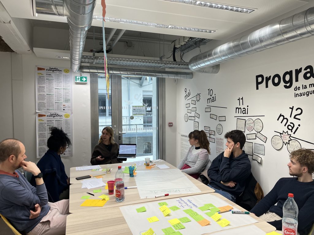 A small group of participants seated around a table, engaged in discussion and working with notes and sticky cards during an interactive workshop session.
