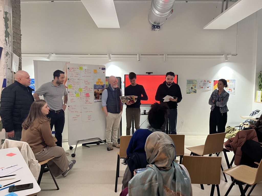 Group photo of participants from an international workshop standing and kneeling together in a classroom space, smiling at the camera.