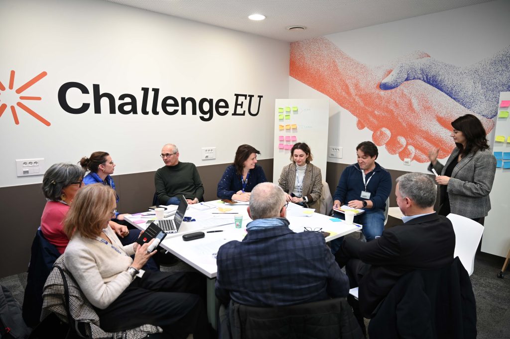 Group discussion during a ChallengeEU session, with participants exchanging ideas around a table and a facilitator guiding the conversation.