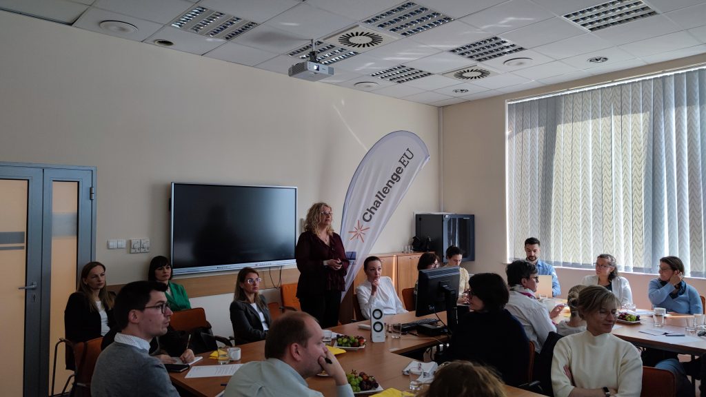 Participants engaged in a discussion during the M.A.R.K.E.T. MeetUp, seated around tables with notes and refreshments, with a ChallengeEU banner visible in the background.