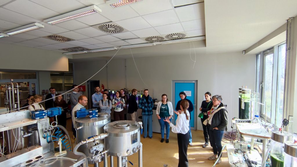 Participants gathered in a laboratory at the University of Warmia and Mazury, listening to a guide explaining environmental engineering equipment used for water treatment and research.