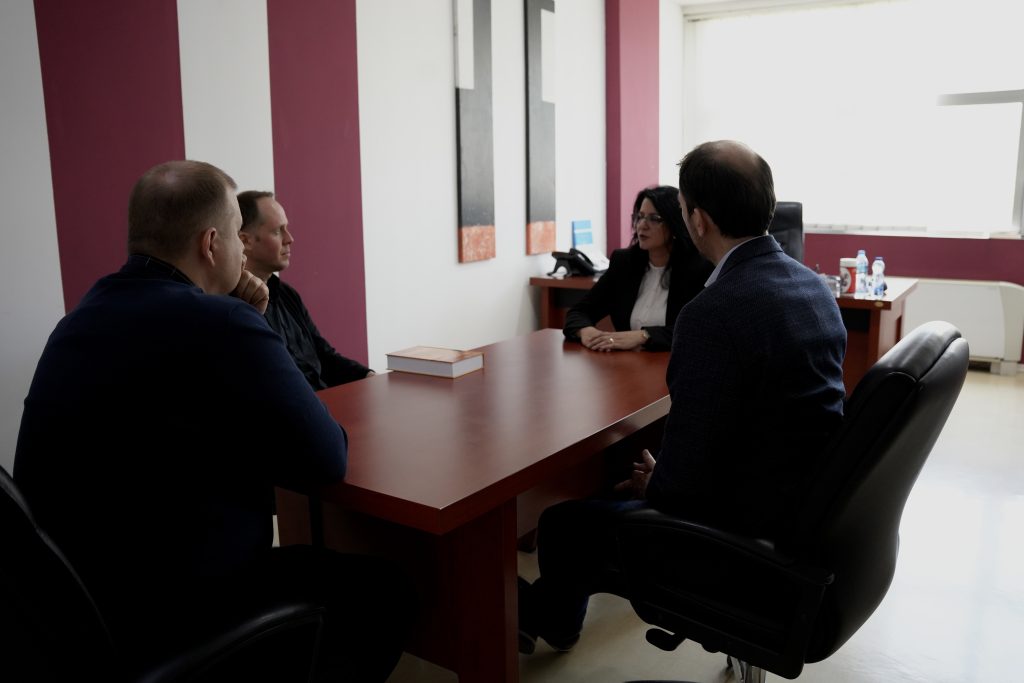 Small group meeting in an office, with participants seated around a table discussing collaboration in a formal setting.