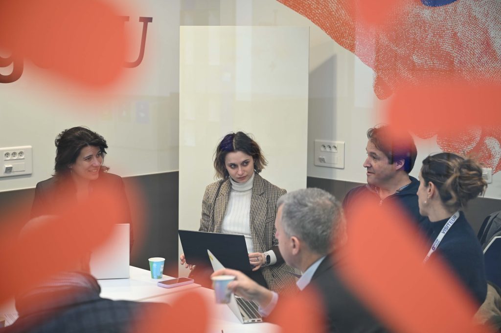 Close-up of participants engaged in discussion during a ChallengeEU session, with laptops and notes on the table, partially framed by the alliance’s visual identity elements.