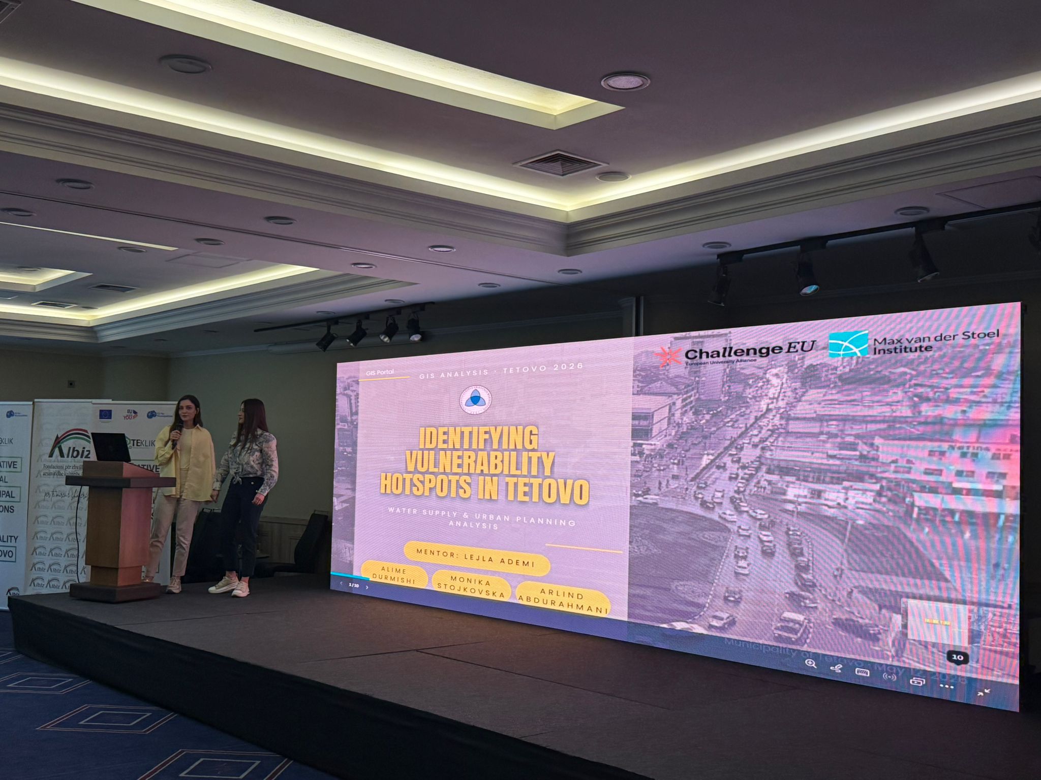 A student presents the GIS project “Identifying Vulnerability Hotspots in Tetovo” on stage, with the ChallengeEU and Max van der Stoel Institute logos displayed on the screen.