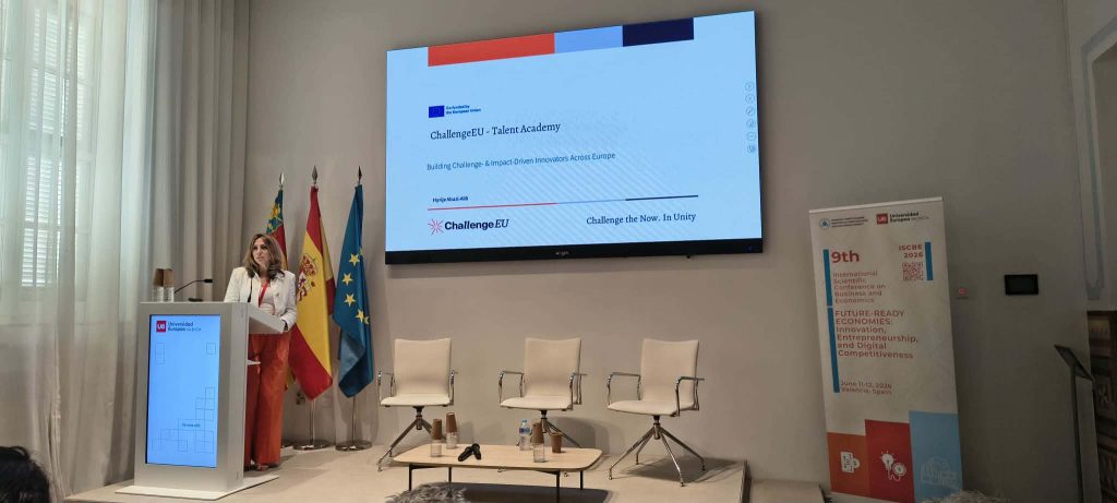 A speaker presents the ChallengeEU Talent Academy during ISCBE 2026, with a presentation slide displayed on a large screen.